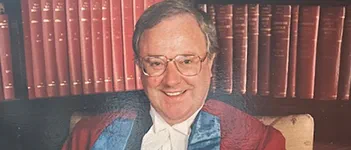 Rodger Pannone, a white man with short dark grey hair and glasses, sits in a library smiling. He wears ceremonial robes.