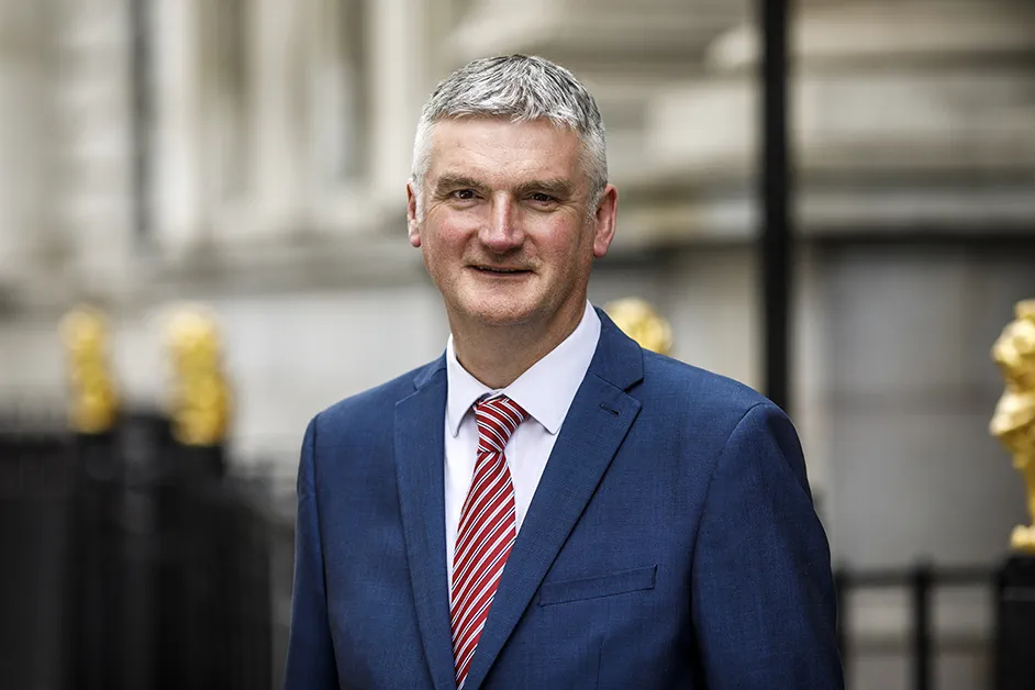 Mark Evans wearing a suit with red tie stands in front of 113 Chancery Lane and smiles