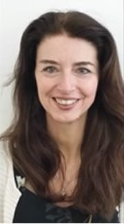 Tracey Burgess is a white woman with long brown hair. She is smiling in front of a plain white background. 
