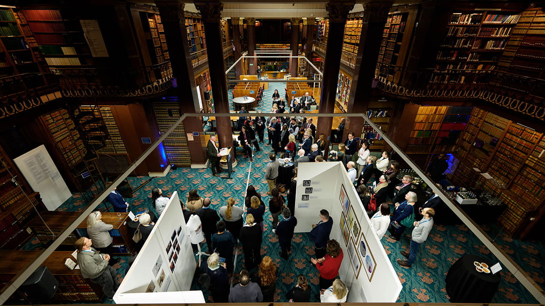 An exhibition of photos in the Law Society library, a group of people are standing around, looking at the art