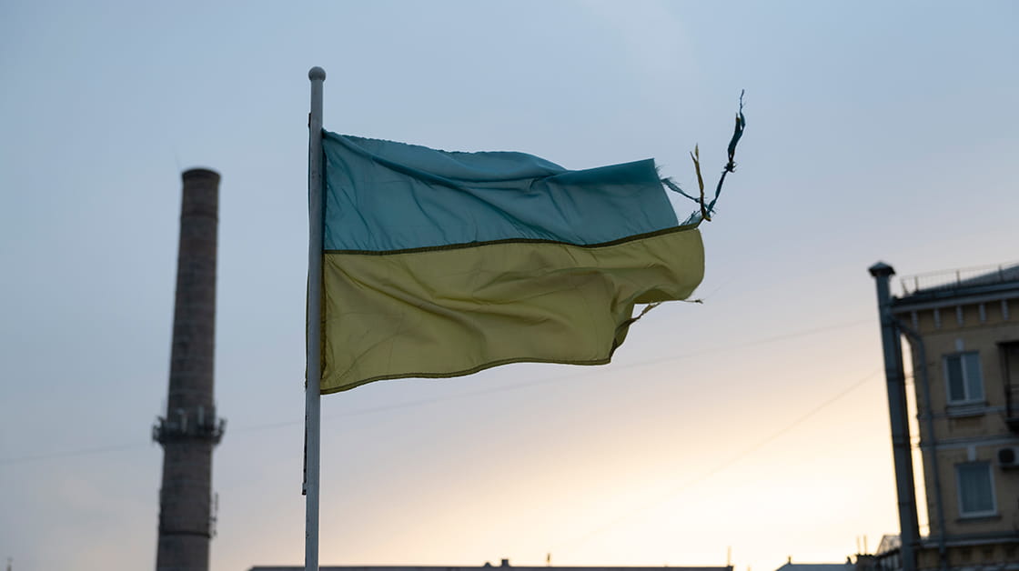 Tattered Ukranian (blue and yellow) flag flying over buildings in Kyiv against pale sky