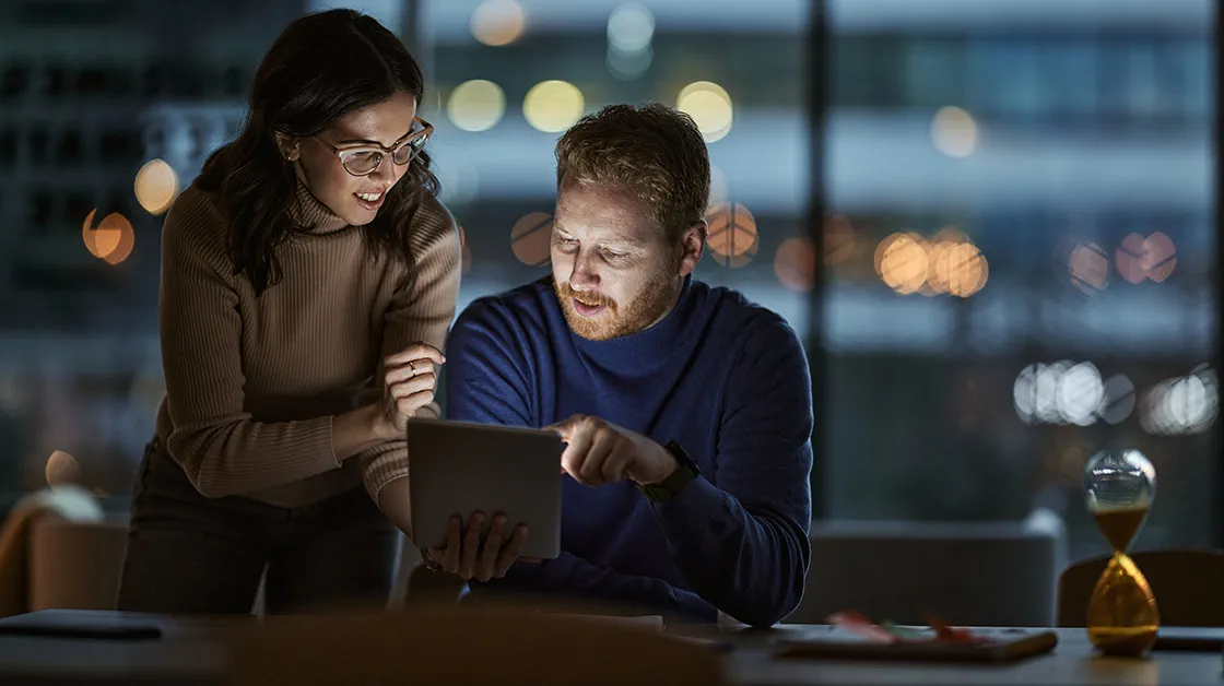Two colleagues stand in an office, looking at information on a tablet