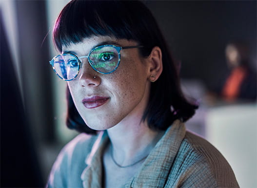 A woman with glasses with reflection of a computer screen on them.