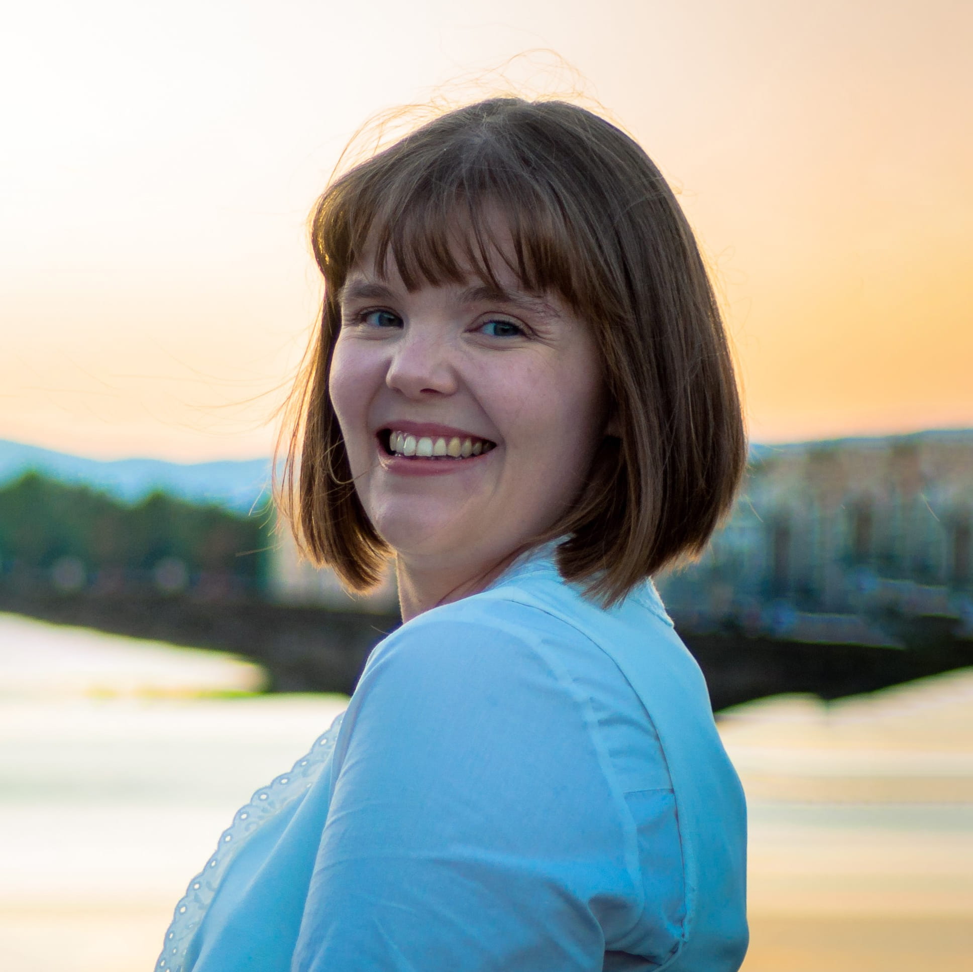 Charlotte Clewes is a white woman with short, straight light brown hair. She is smiling widely and wears a white blouse.