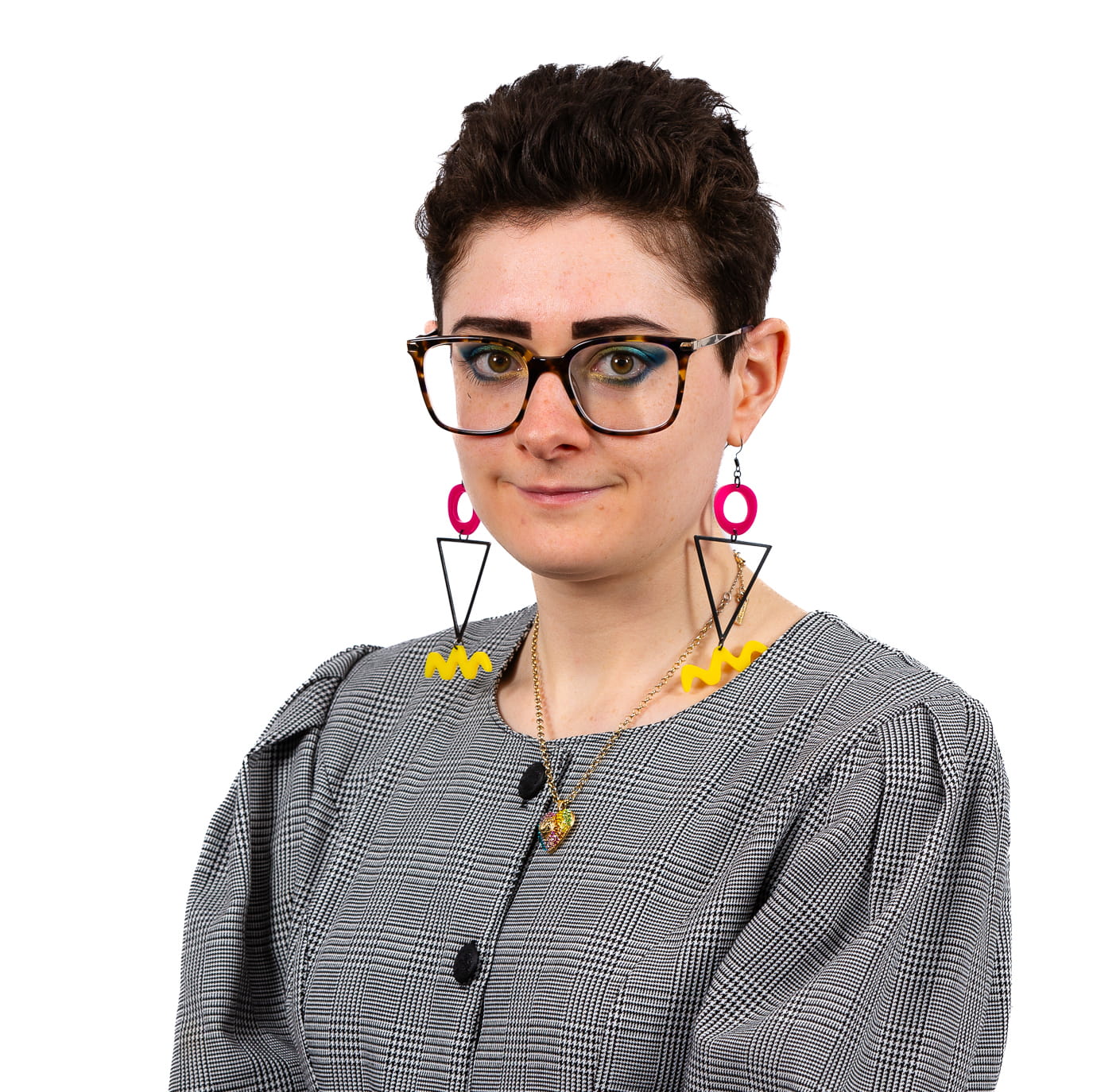 Concetta Dalziel is a white woman with short, curly dark brown hair. She is smiling and wears a black-and-white tartan shirt, dark framed glasses and long dangly earrings, composed of pink circles, black triangles and yellow squiggles.