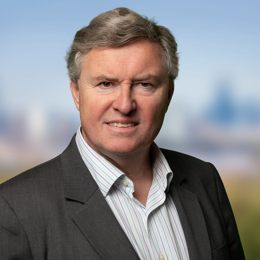 Duncan McNair is a white man with short dark grey hair. He is smiling and wears a dark grey suit over an open-collar white shirt.