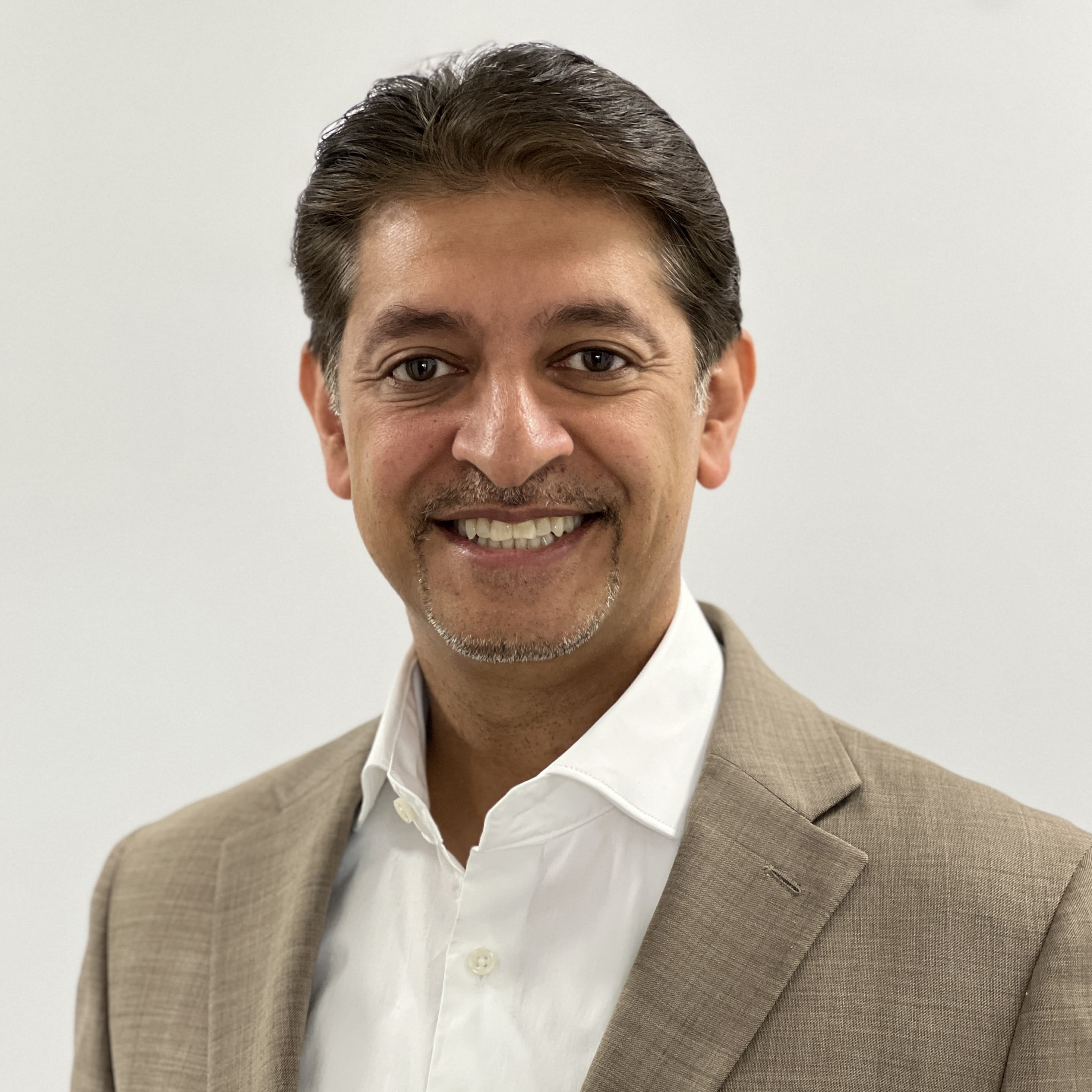 Khalil Yousuf is a man with short, wavy black hair. He is smiling widely and wears a light brown suit and a white open collar shirt.