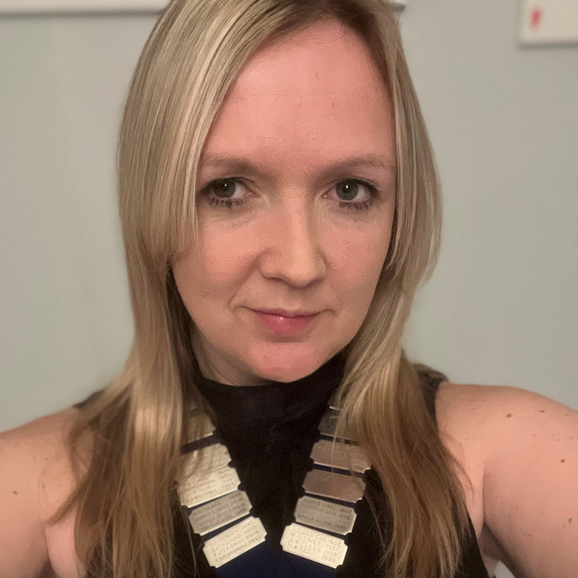 Kirsty Richards is a white woman with long, straight blonde hair. She is smiling and wears a black sleeveless top with a ribbon of gold medals around her neck.