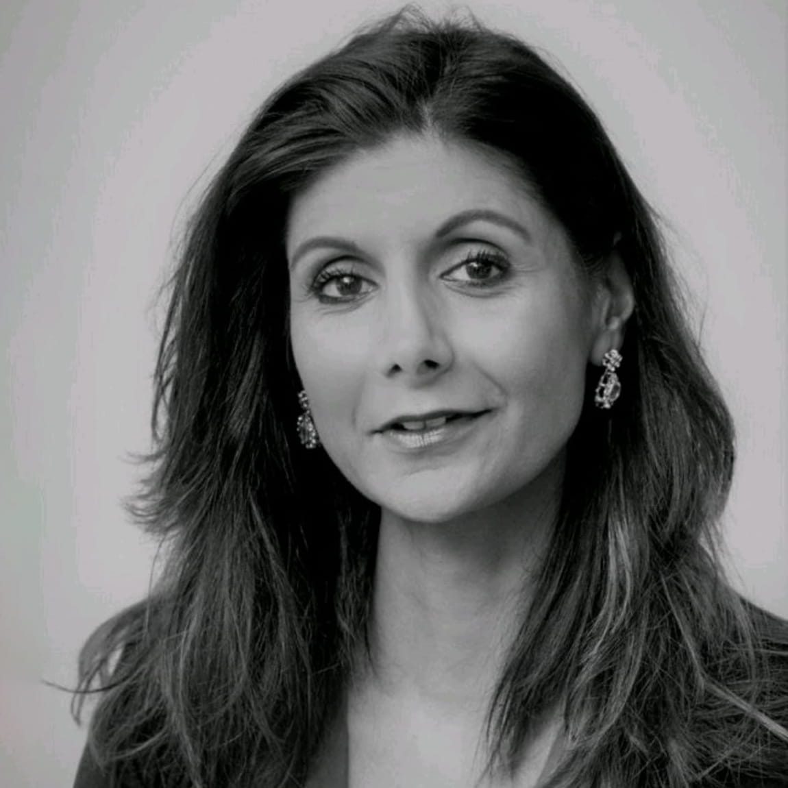 Sharon Benning is a white woman with long, wavy dark hair. She is smiling and wears a dark blazer and earrings.