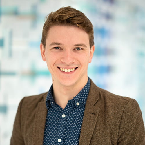 Harry Clark smiles, wearing a tweed suit and open-collar navy shirt.
