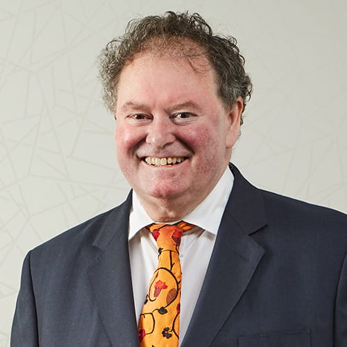 Mark Stephens CBE smiling, wearing a dark grey suit and orange tie.