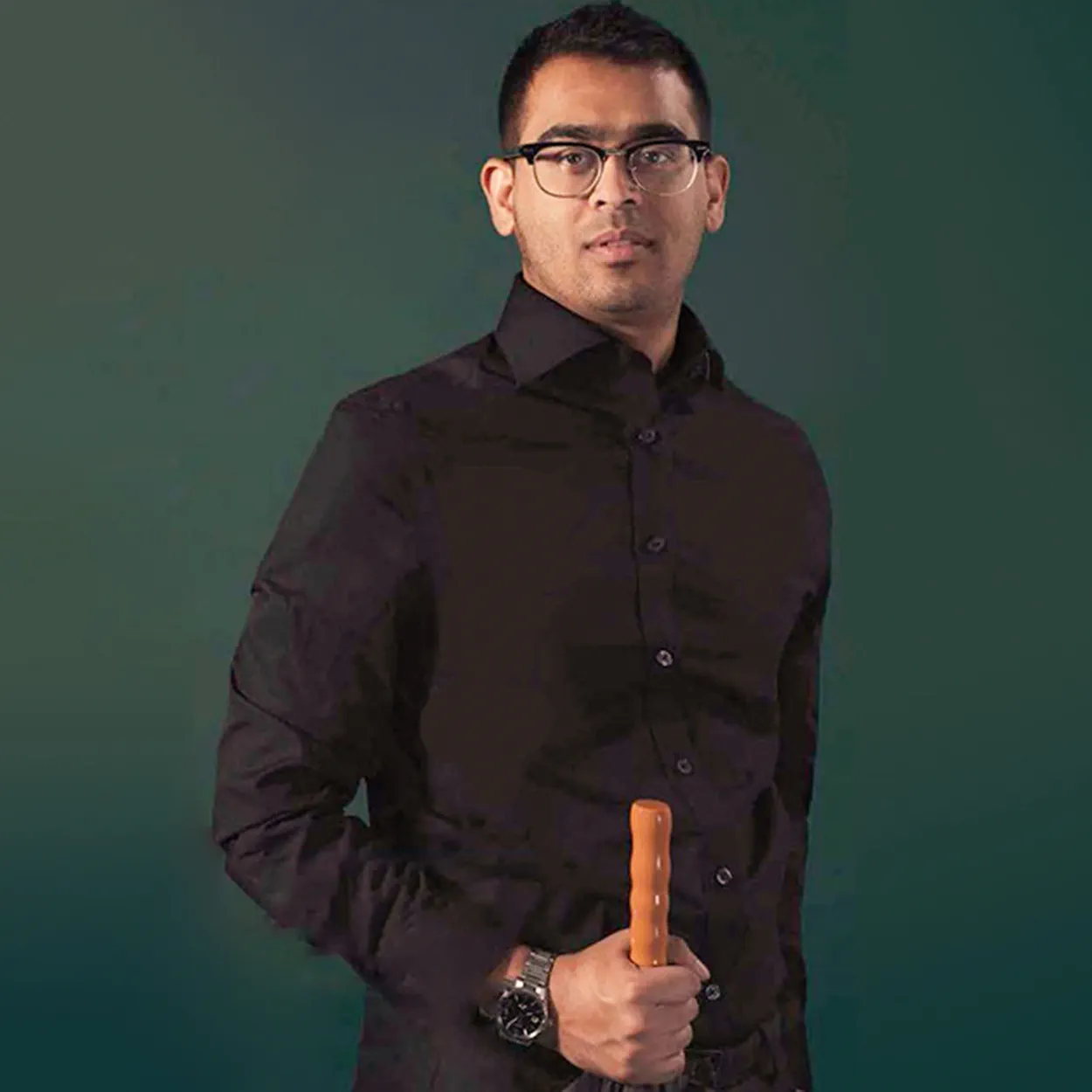 Kawsar Zaman is a man of South Asian heritage. He holds an umbrella and wears glasses, a black shirt and a silver watch.