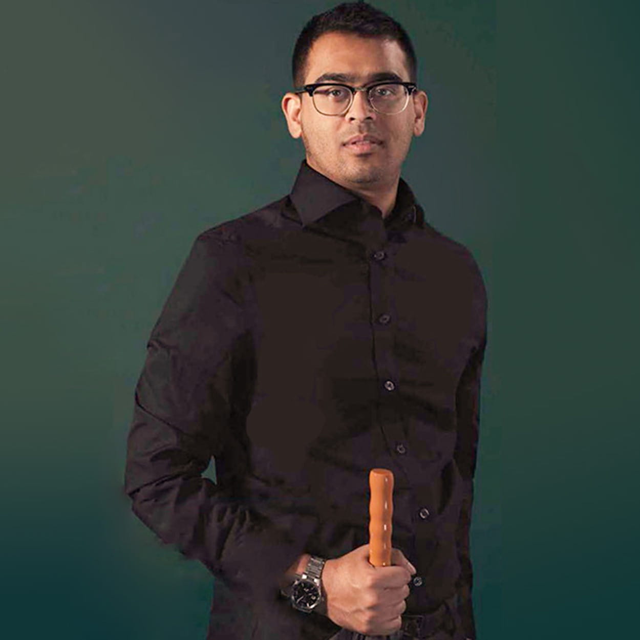 Kawsar Zaman is a man of South Asian heritage. He holds an umbrella and wears glasses, a black shirt and a silver watch.