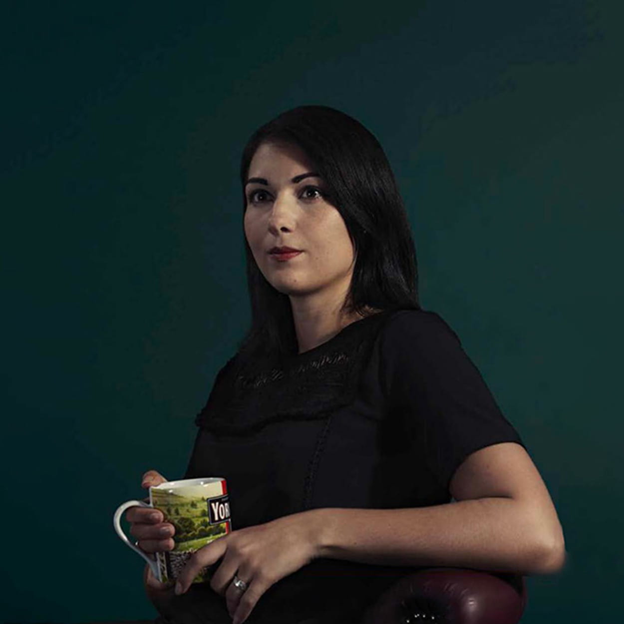 Kira Wilkinson is a white woman with medium-length, straight dark brown hair. She wears a black dress and holds a mug of Yorkshire Tea.