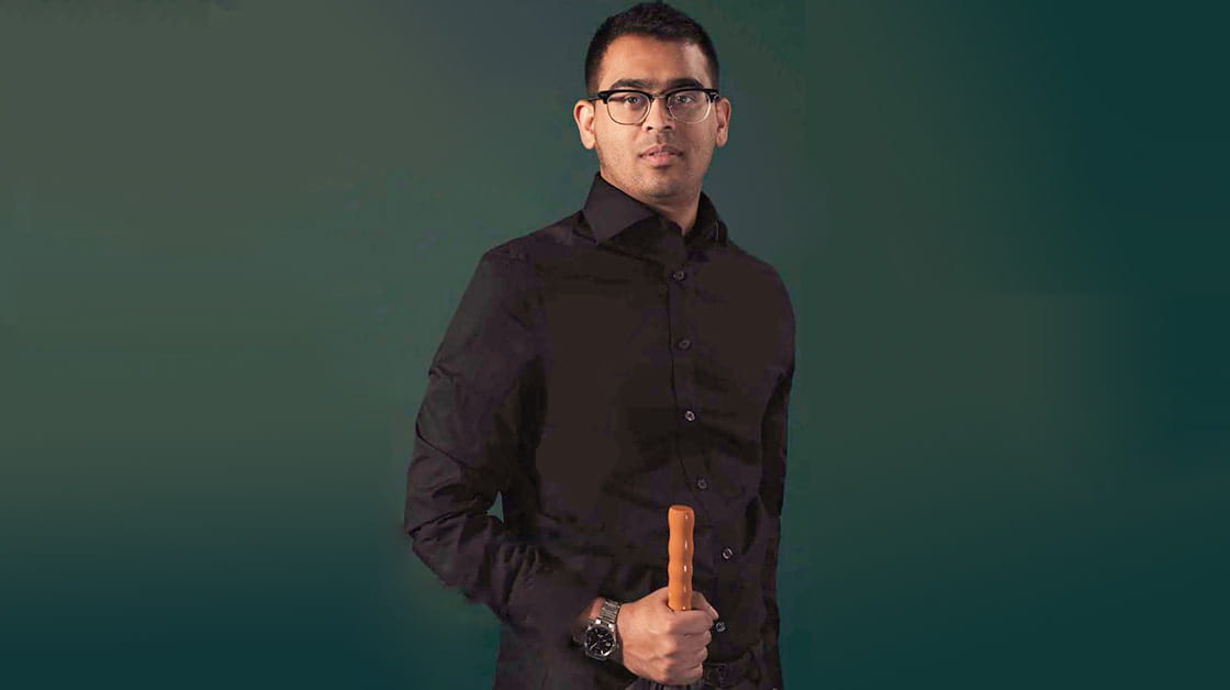 Kawsar Zaman is a man of South Asian heritage. He holds an umbrella and wears glasses, a black shirt and a silver watch.