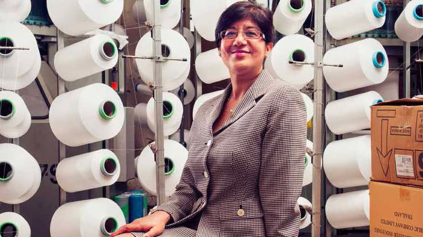 Shama Gupta is a woman of South Asian heritage with short, straight, dark brown hair. She is smiling and wears glasses and a light brown tweed suit.