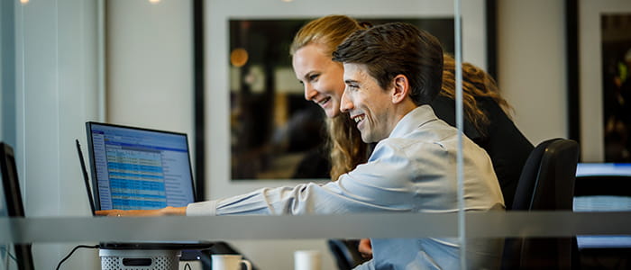 Two solicitors smile looking at a computer screen.