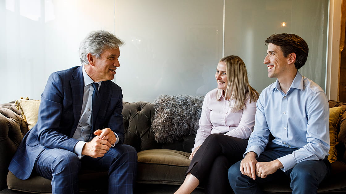 A solicitor sits on a sofa speaking with two clients