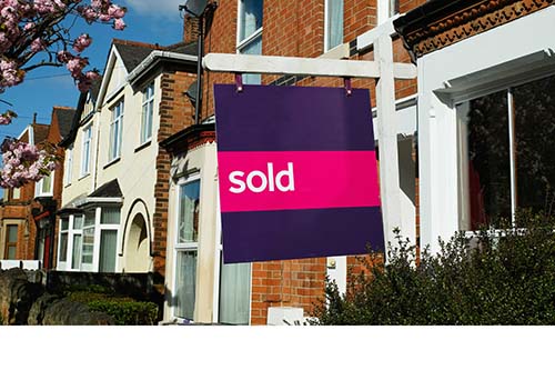 Sold sign outside red-brick terrace house on sunny spring day