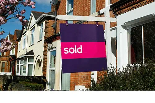 Sold sign outside red-brick terrace house on sunny spring day