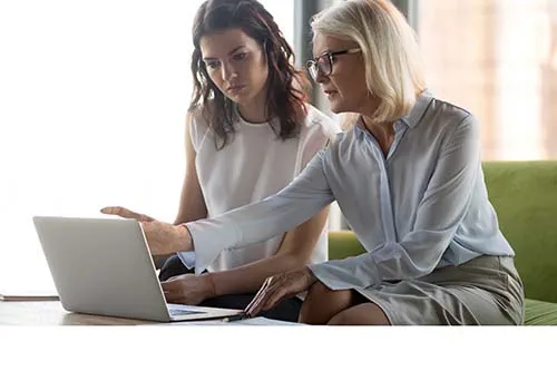 Two professional women looking at laptop, one is pointing at screen, looking concerned