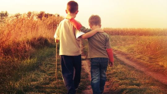 Two boys walking through grass