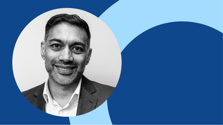 A black and white photo on a blue background, of an Asian man, smiling, wearing a black jacket and white shirt. 