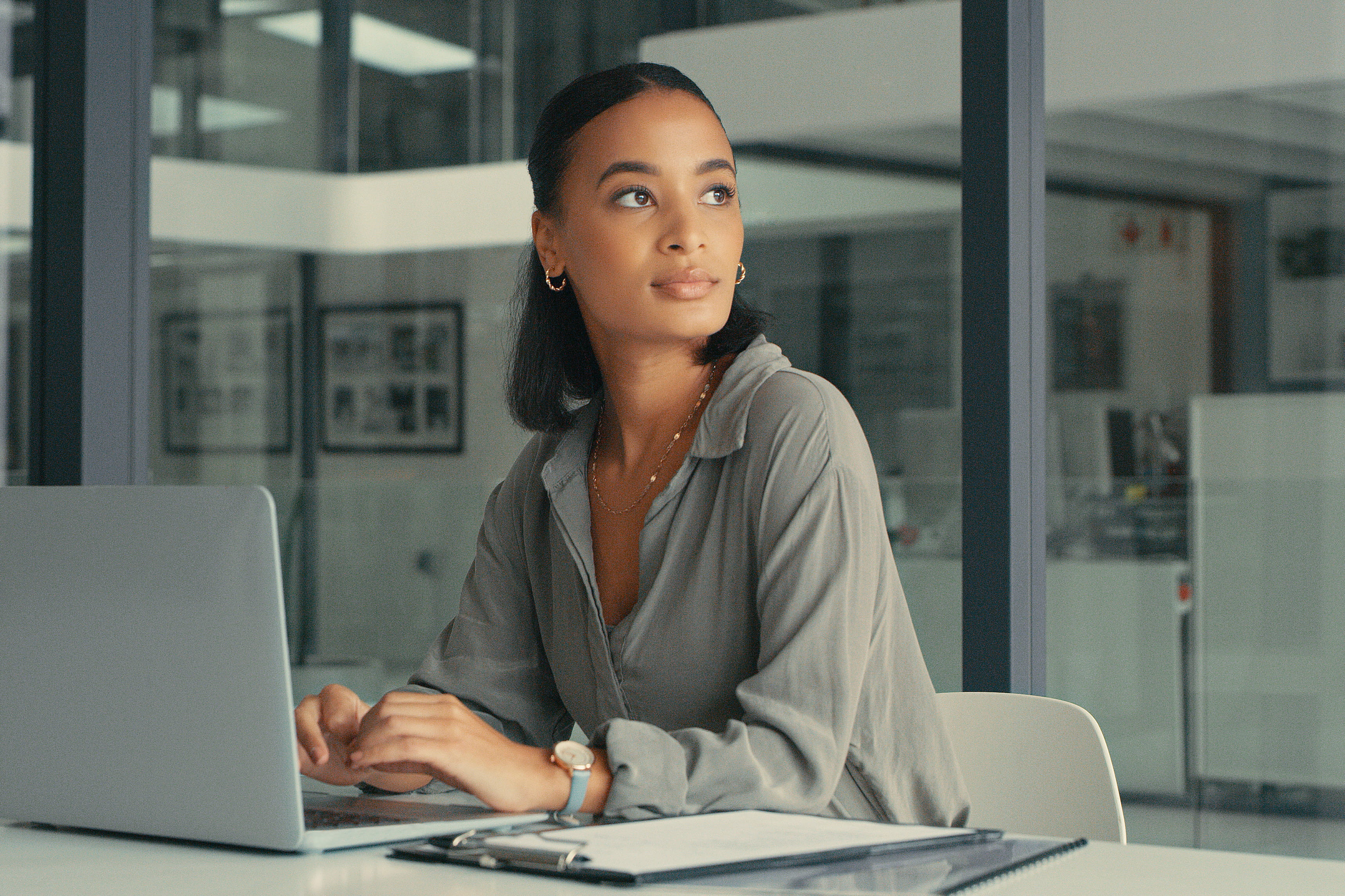 A woman using a laptop in an office stares into the distance.