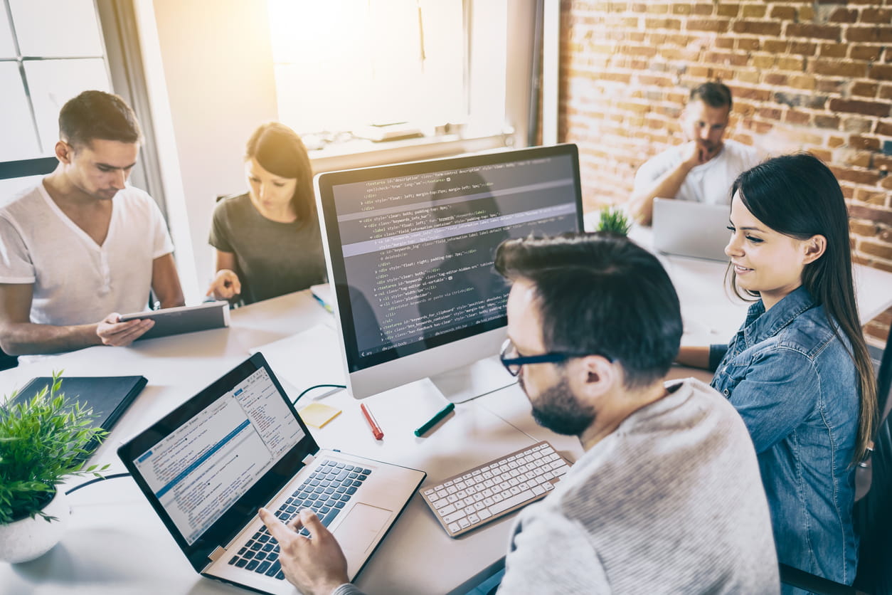 A group of men and women gather around computers. 