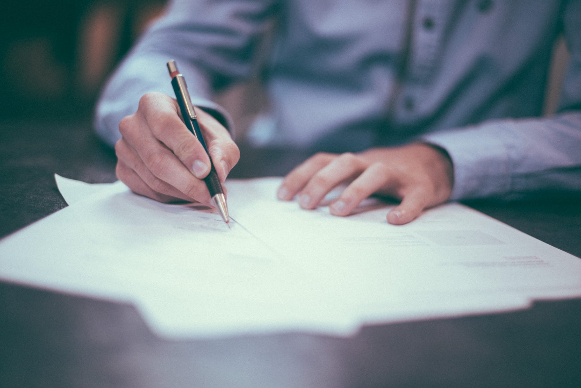 Someone in a blue shirt, writing with a fountain pen on a piece of paper