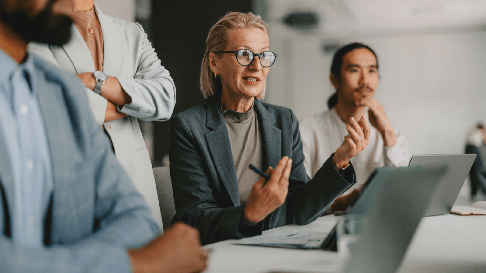 Female professional with glasses sitting down leading a meeting with group of colleagues 