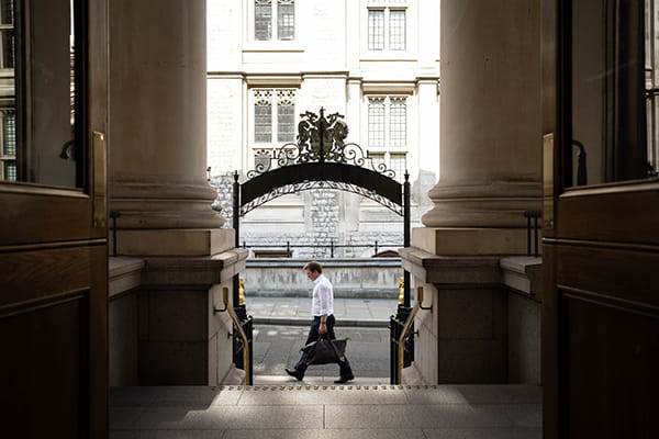 Man in white shirt and black trousers, carrying a black duffel bag is walking on Chancery Lane underneath the Law Society archway
