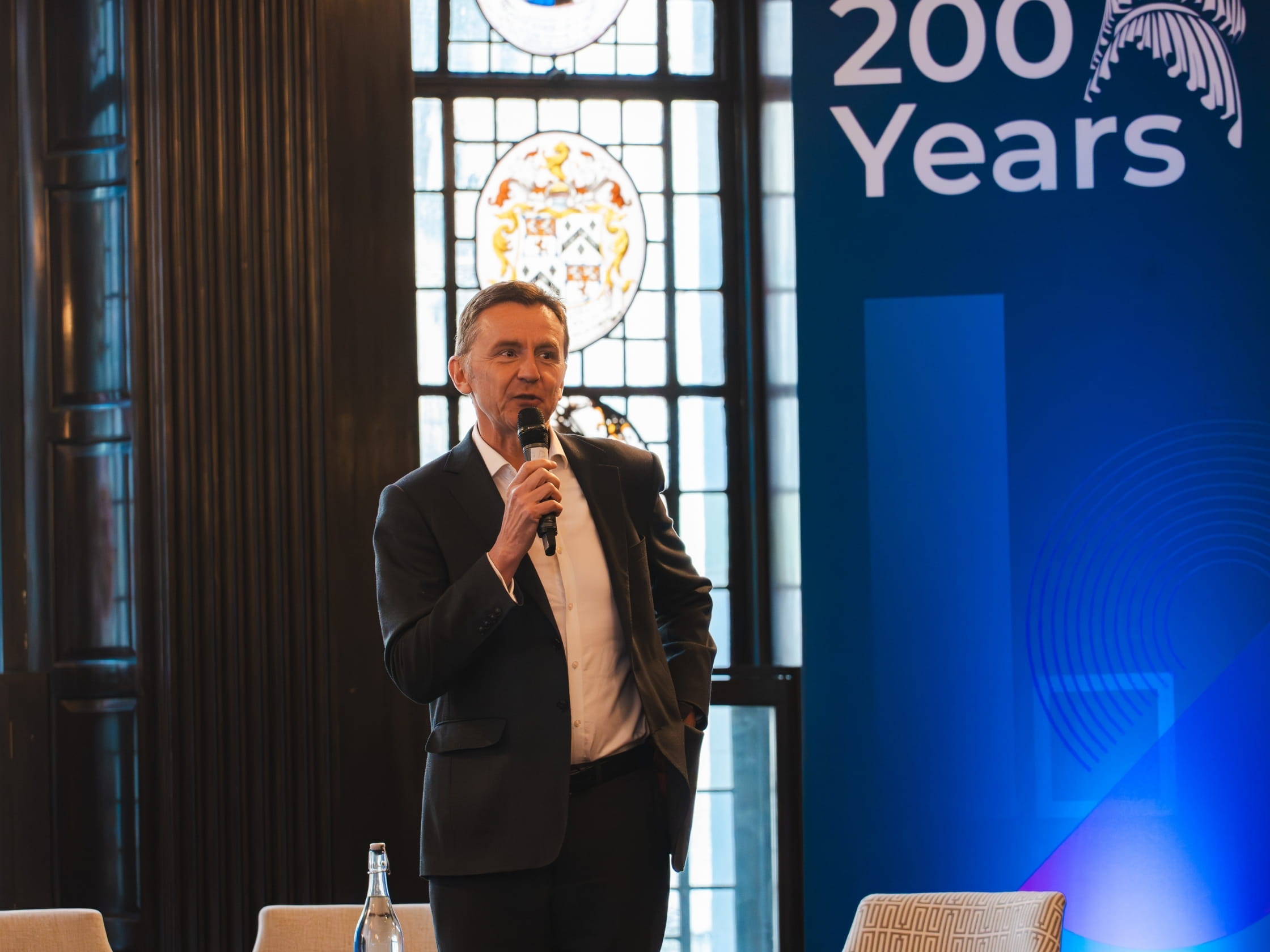Ian Jeffery holding a microphone, on stage in front of a banner.