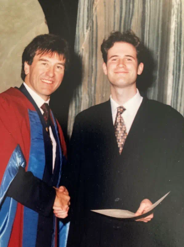 A man in a gown shakes the hand of Ben who is holding a certificate.
