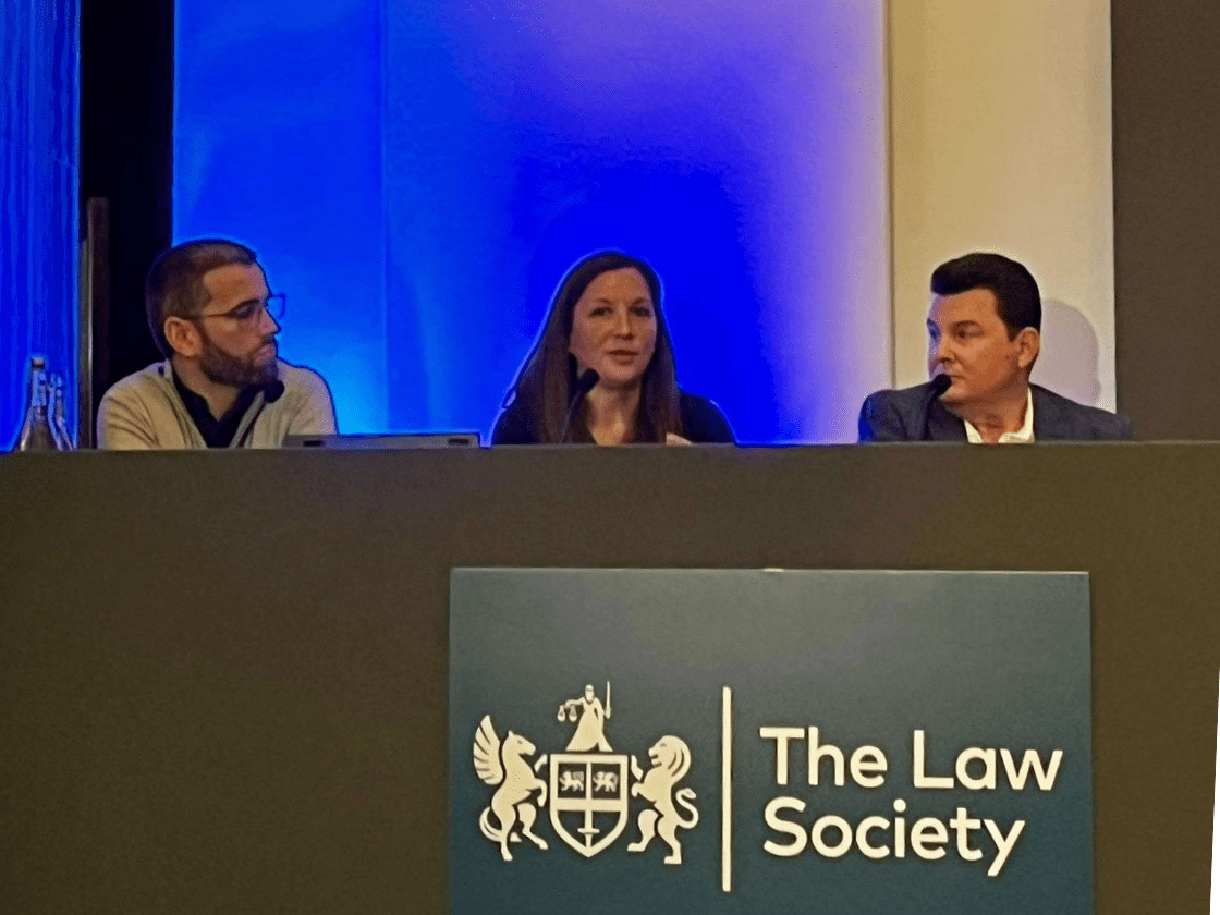 A woman speaks on a panel, with two other guests.
