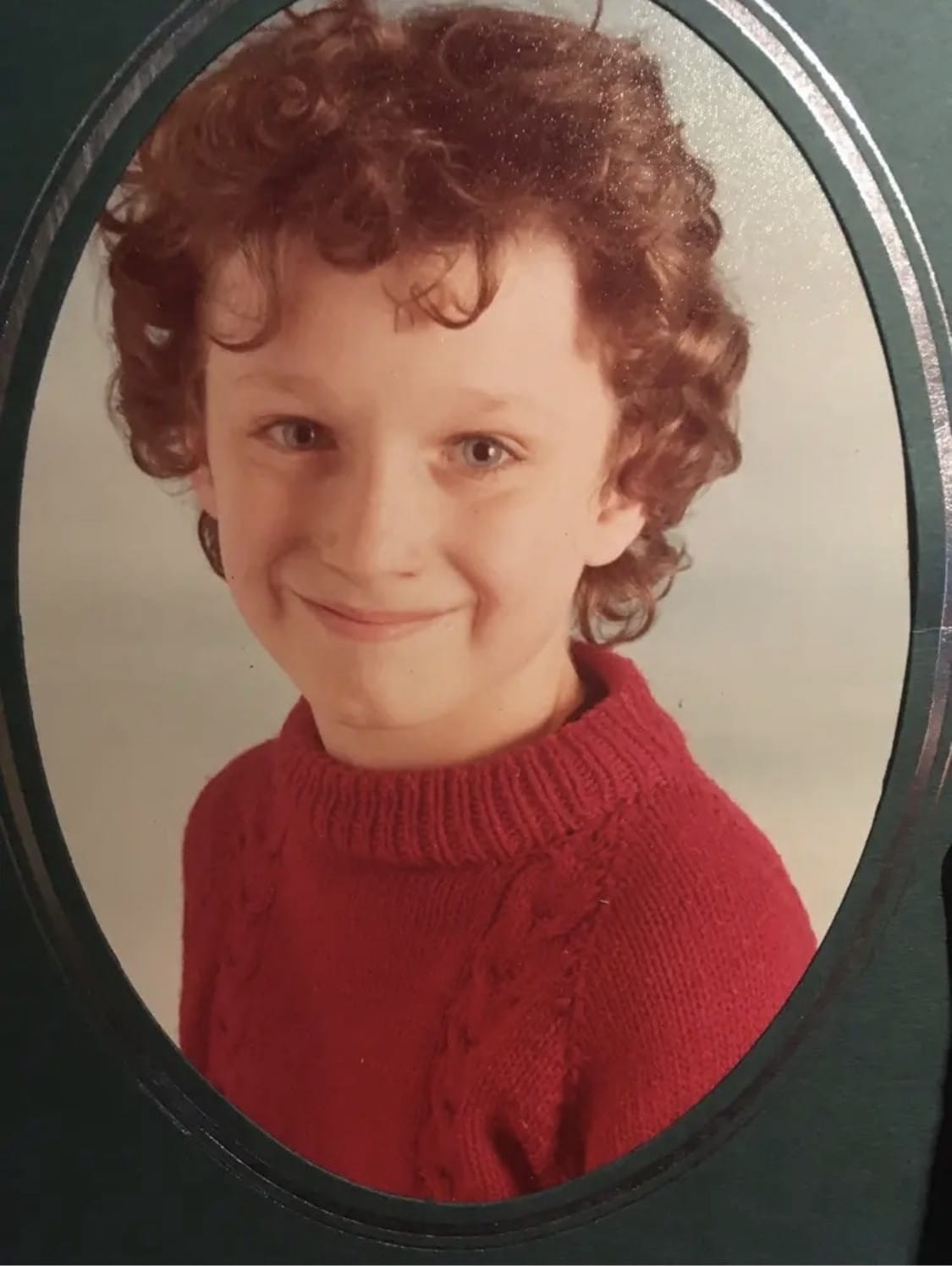 A young boy with brown curly hair wears a red jumper in this photo of Gary Haines as a child