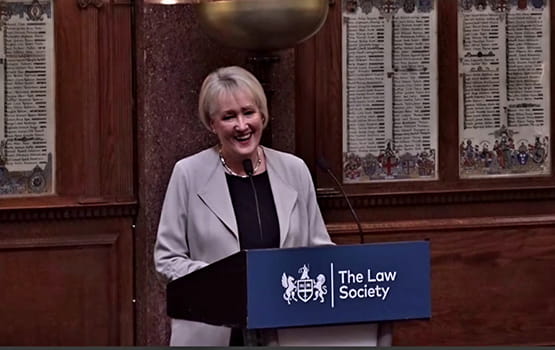 Carolyn Kirby giving a speech at a lectern with the Law Society logo.