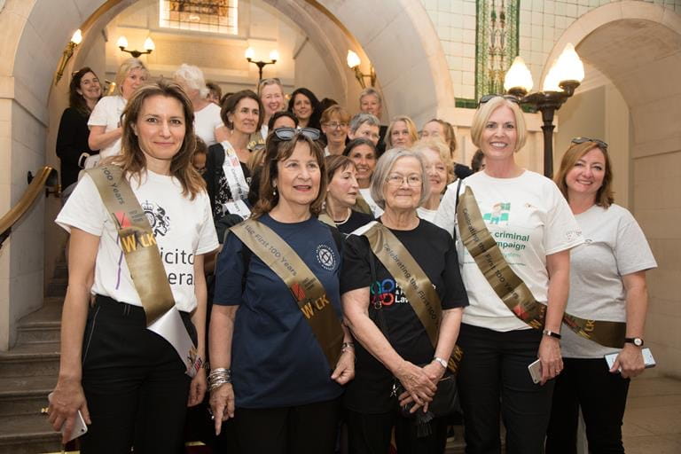 A group of people standing on a staircase, wearing gold sashes.