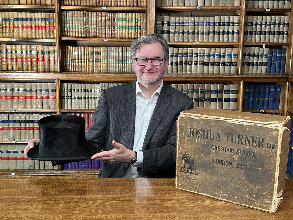Archivist Gary Haines smiles in the library with a top hat that is one of the artefacts in the Law Society archive