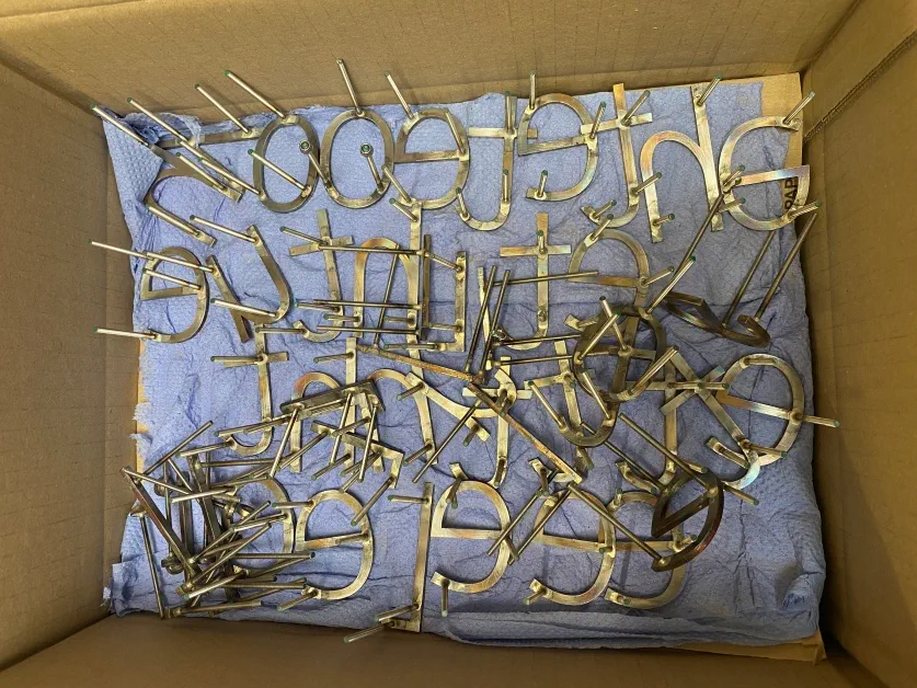 A cardboard box lined with blue tissue and covered in steel letters that are being prepared for an artwork