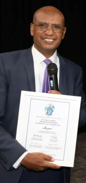 Person in a suit smiling and holding a certificate, posing for a formal photo.