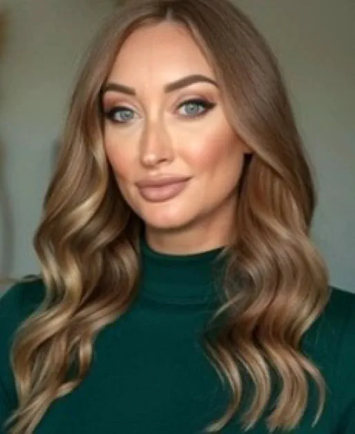 Individual with long brown hair wearing a green top, posing for a portrait-style photo.