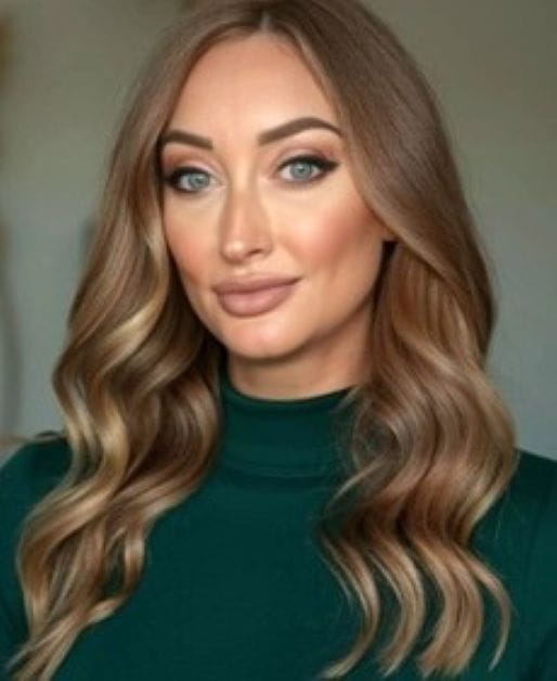 Individual with long brown hair wearing a green top, posing for a portrait-style photo.