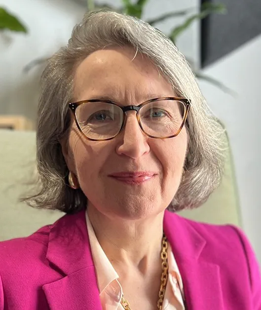Person with short hair and glasses wearing a pink jacket, smiling at the camera.