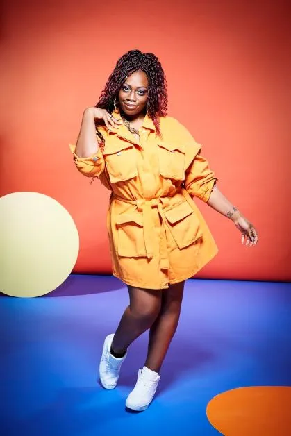 Immigration solicitor and comedian Sikisa poses in a bright orange dress