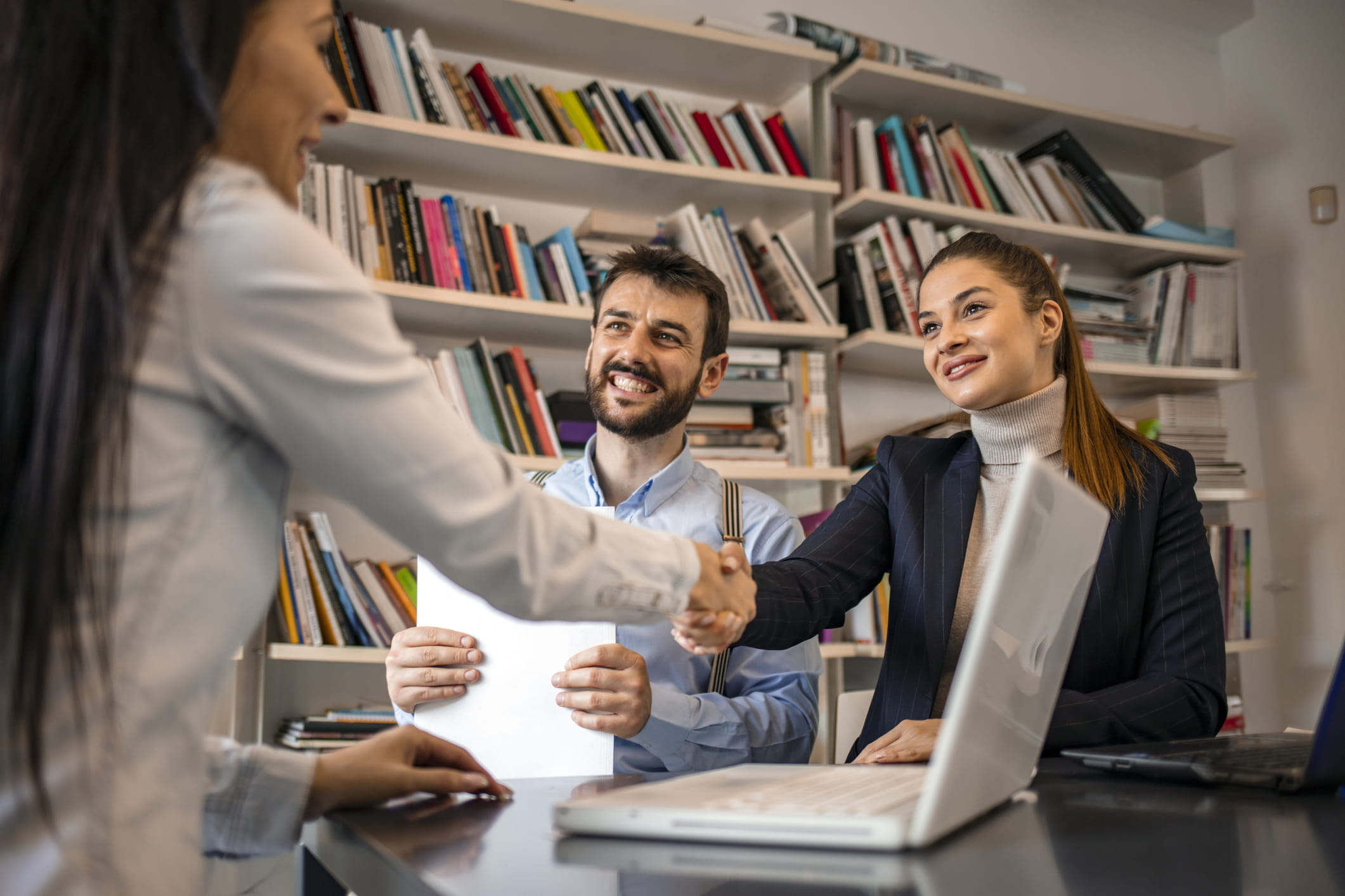 Business woman shaking hand to her female partner while sitting in the office. 