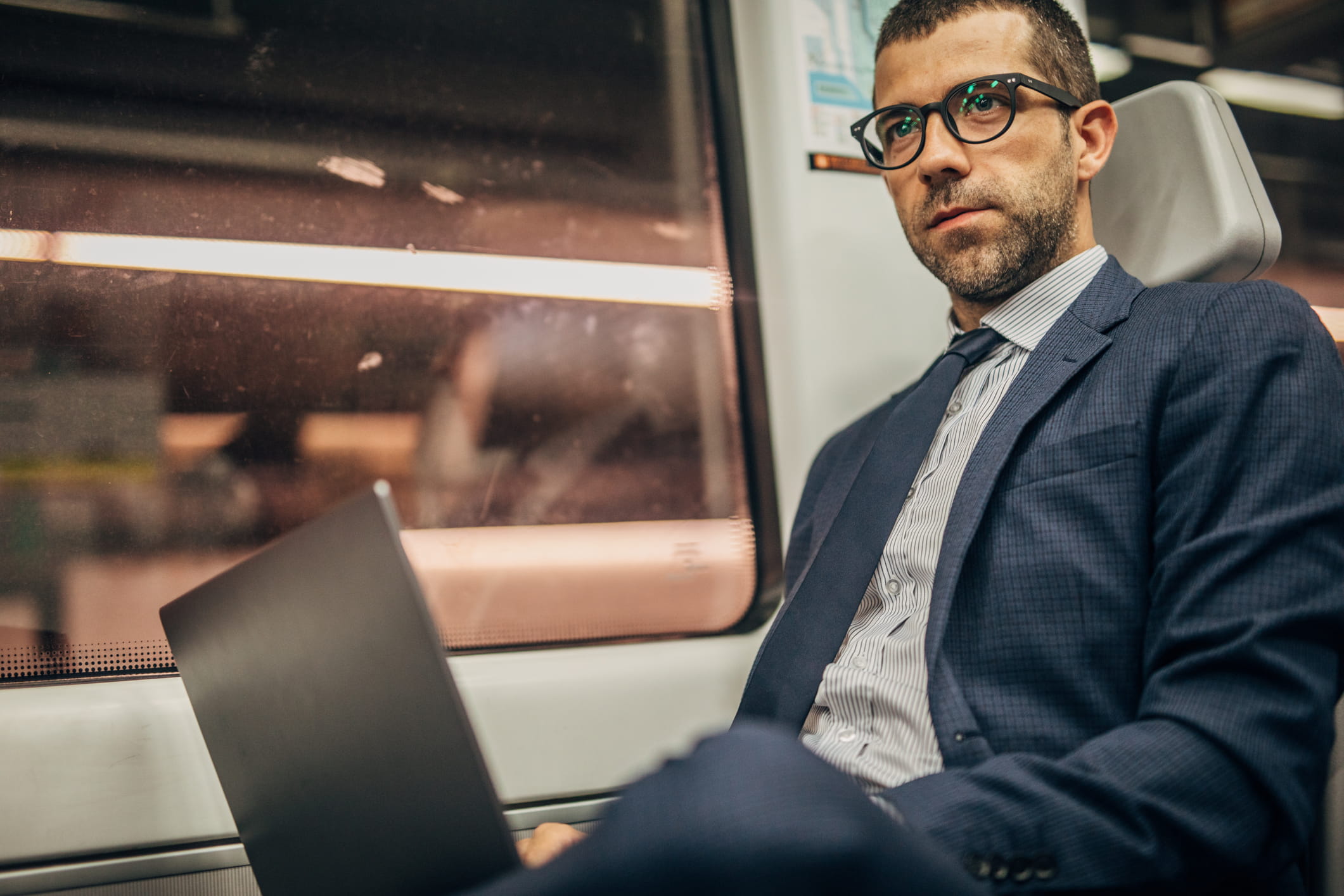 A man sat own a train with a laptop looks up, as if overhearing a conversation.
