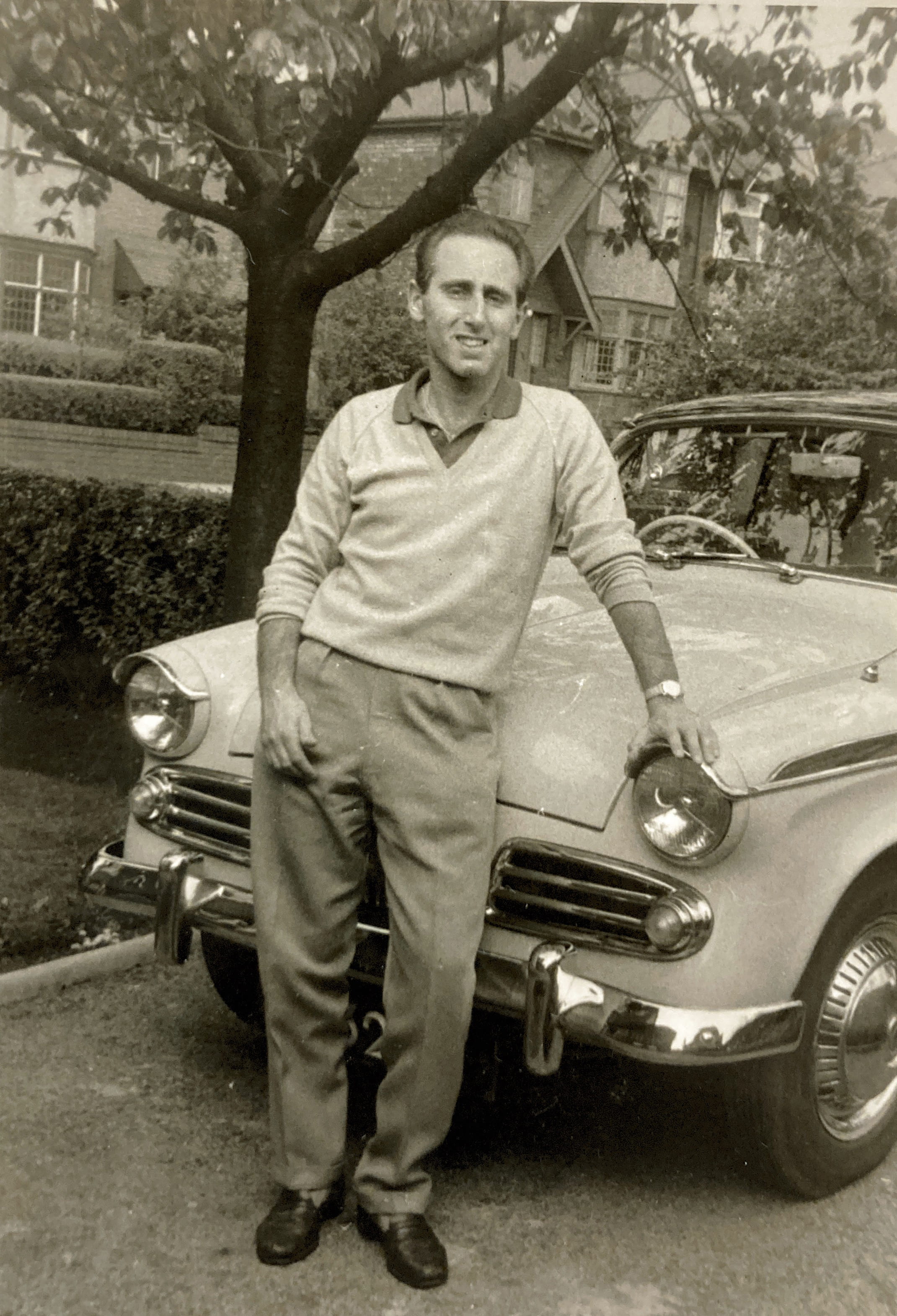 A man poses with a 1950s vintage car.