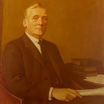 Portrait of former Law Society President Sir Ernest Bird. He is grey haired man wearing a suit whilst sat at a desk with lots of books