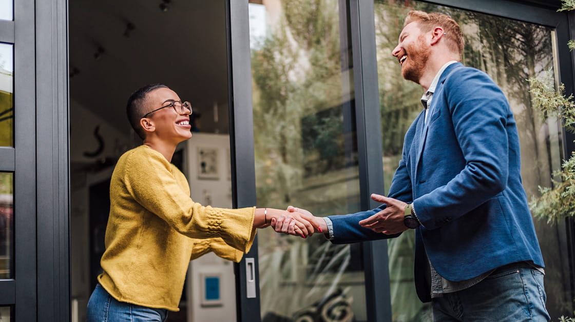 A woman shakes hands with a man at the entrance to an office.
